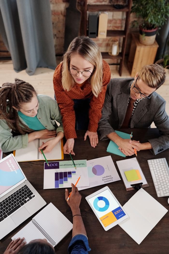 Mastering the First Impression: Your intriguing post title goes here Top view of a diverse group discussing business reports and charts around a desk.
